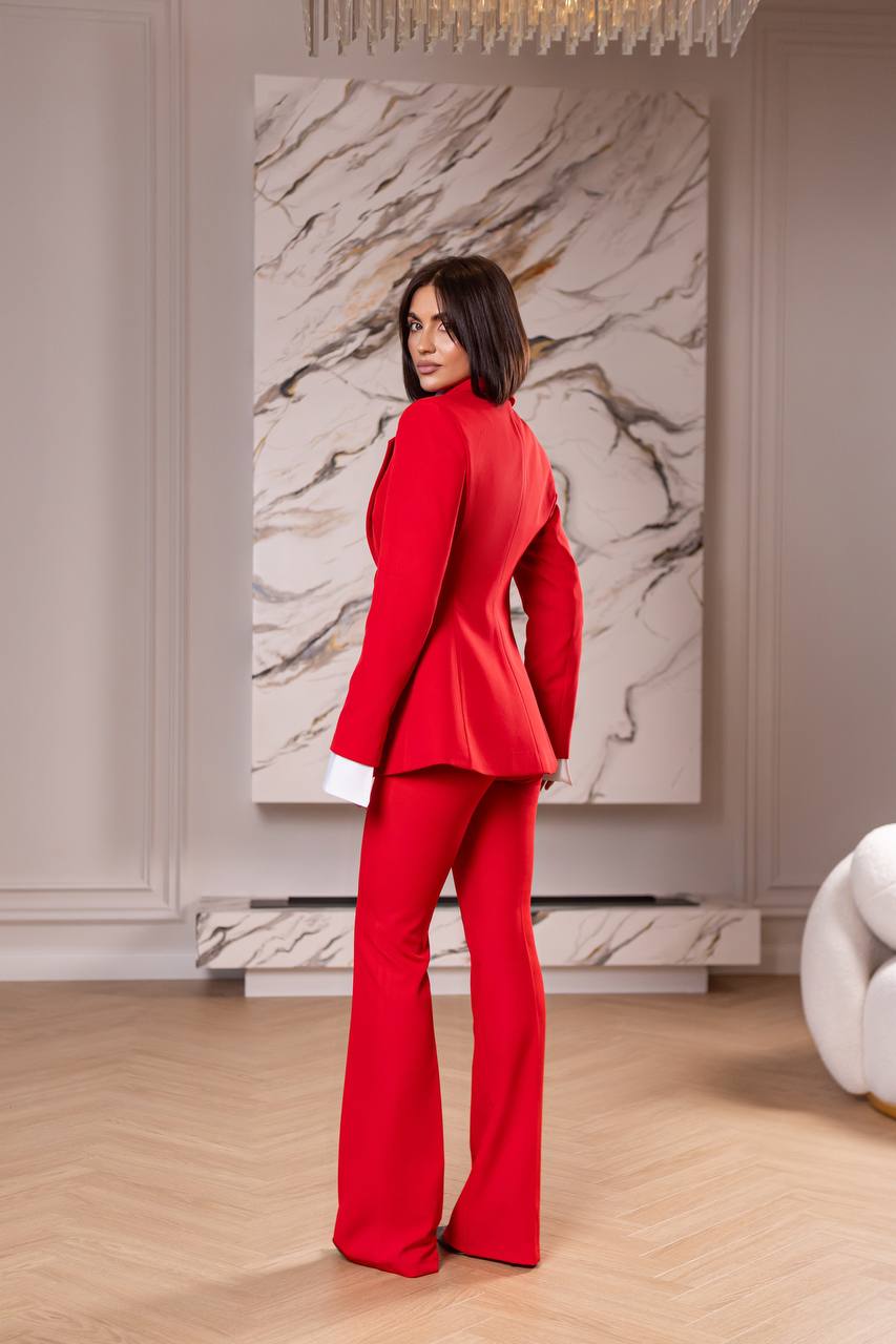 Woman in a red suit standing in a room with a marble wall and chandelier.