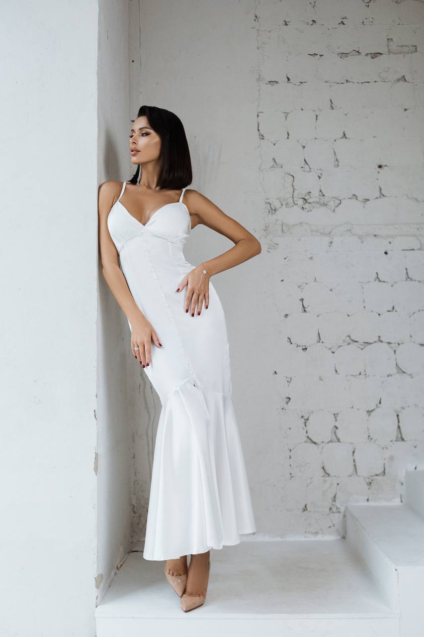 Woman in a white dress standing against a textured white wall.