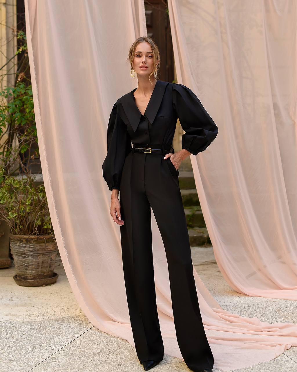 Woman in a black outfit standing in front of pink curtains