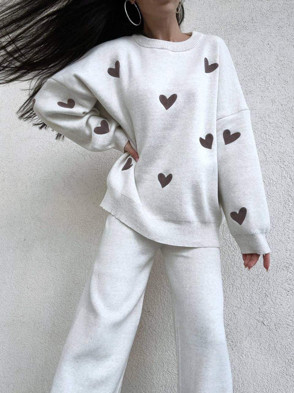 White sweatshirt with brown heart patterns worn by a person against a plain background