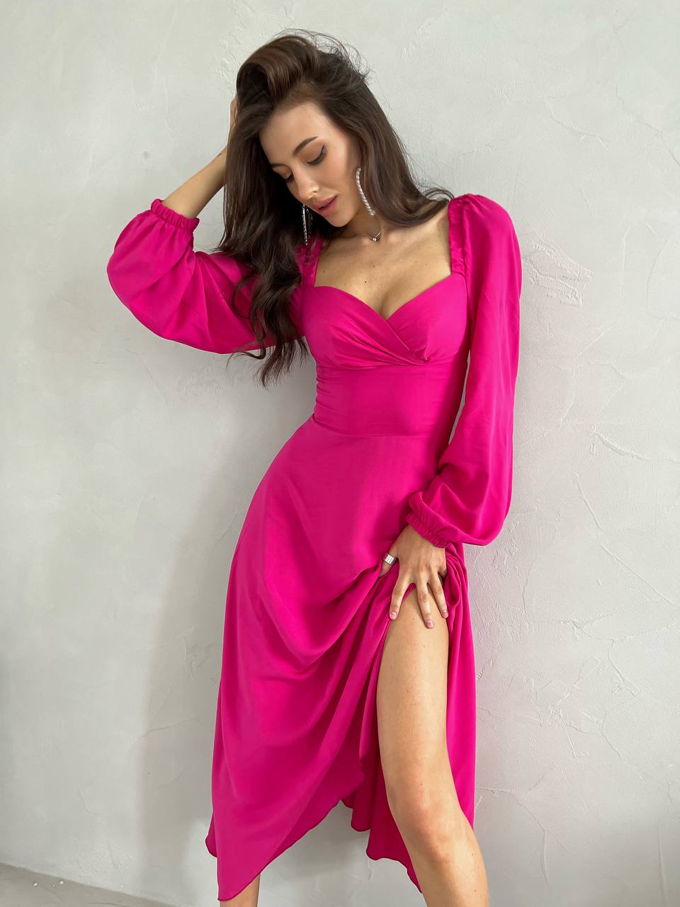 Woman wearing a bright pink dress with long sleeves against a plain background