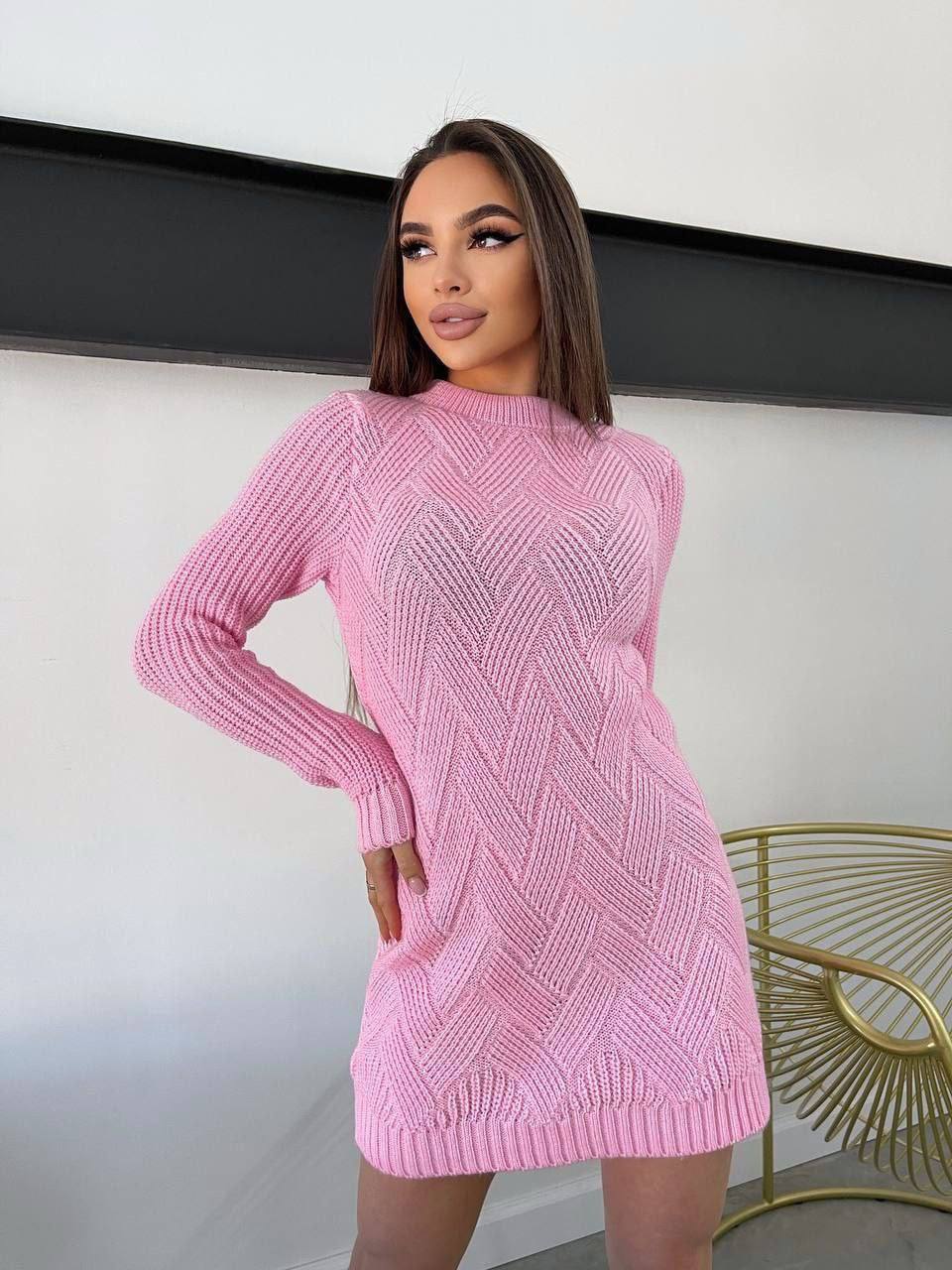 Woman wearing a pink knitted dress against a white wall.