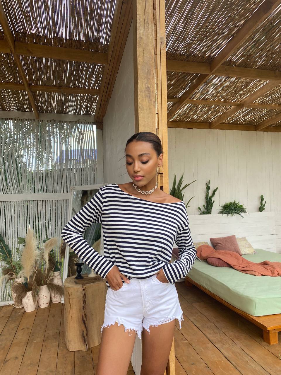 Woman wearing a black and white striped top and white shorts in a wooden interior setting.