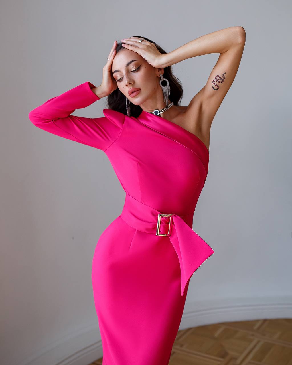 Woman wearing a bright pink one-shoulder dress with a belt against a neutral background