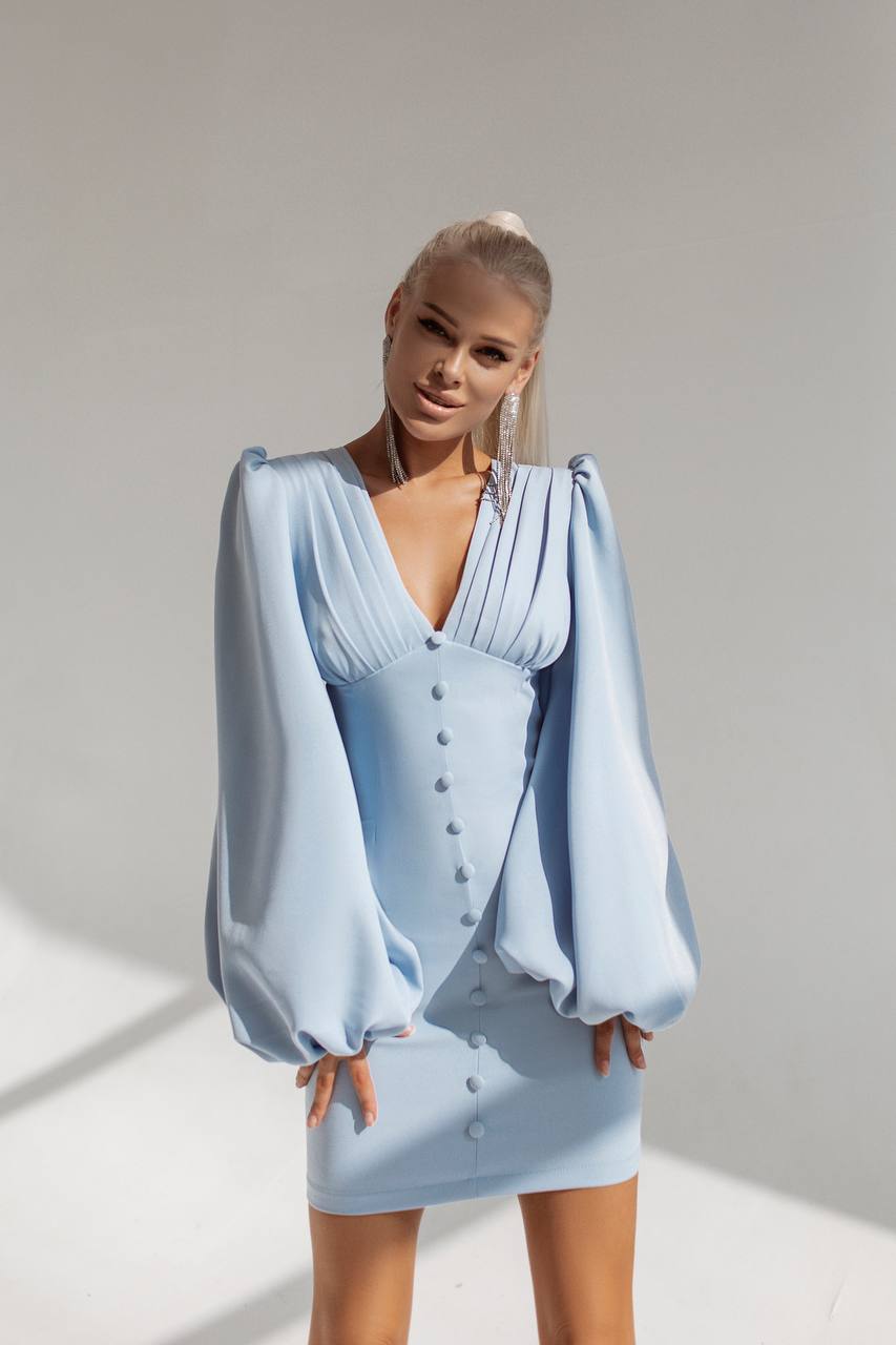 Woman wearing a light blue dress with puffed sleeves against a plain background