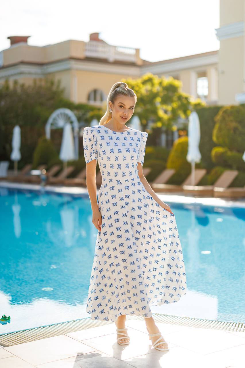 Woman in a white dress with blue patterns standing by a pool