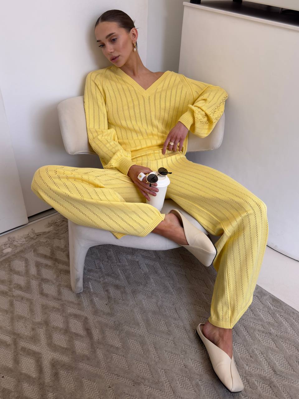 Woman in a yellow outfit sitting on a white chair in a minimalistic room.