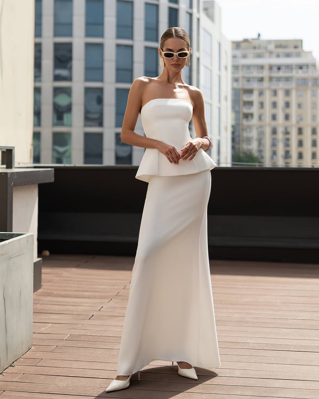 Woman in a white strapless dress standing on a rooftop with cityscape background