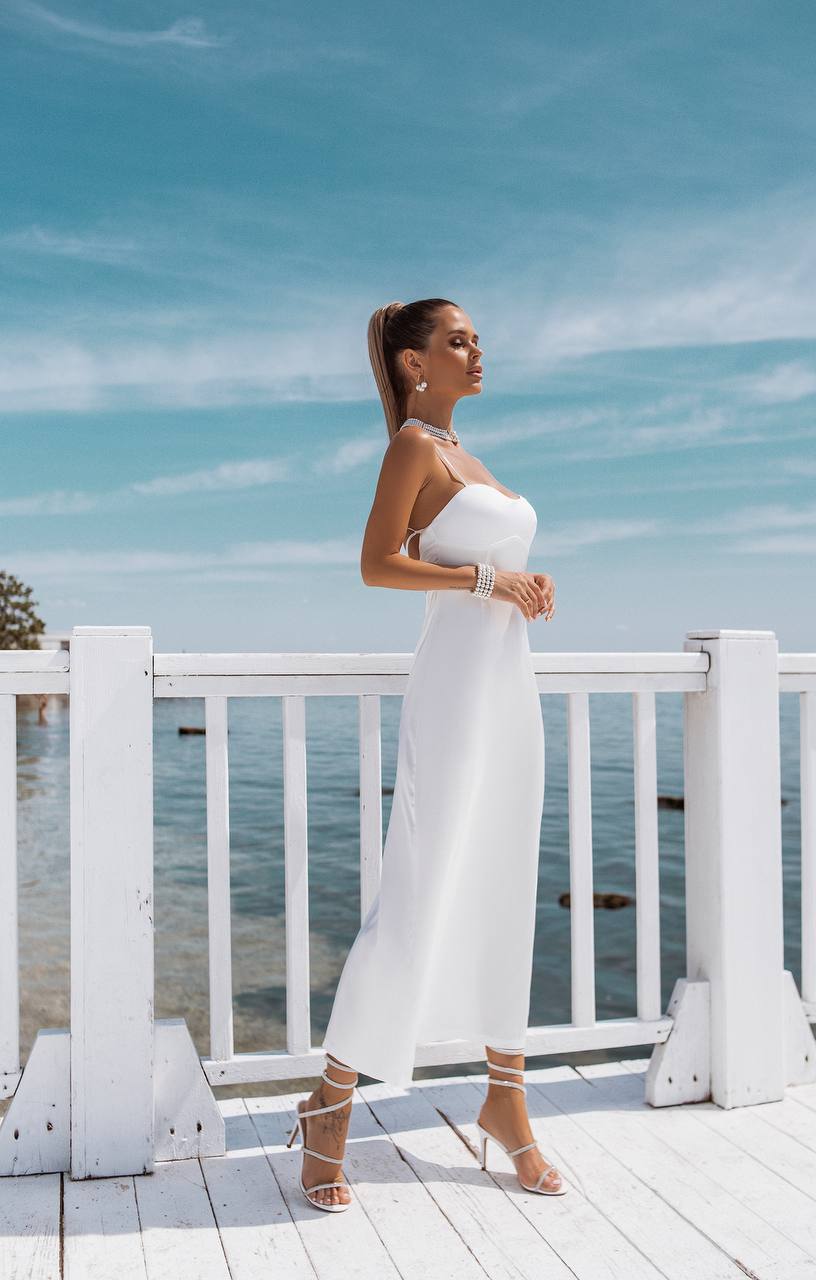 Woman in a white strapless dress standing on a wooden deck by the sea.