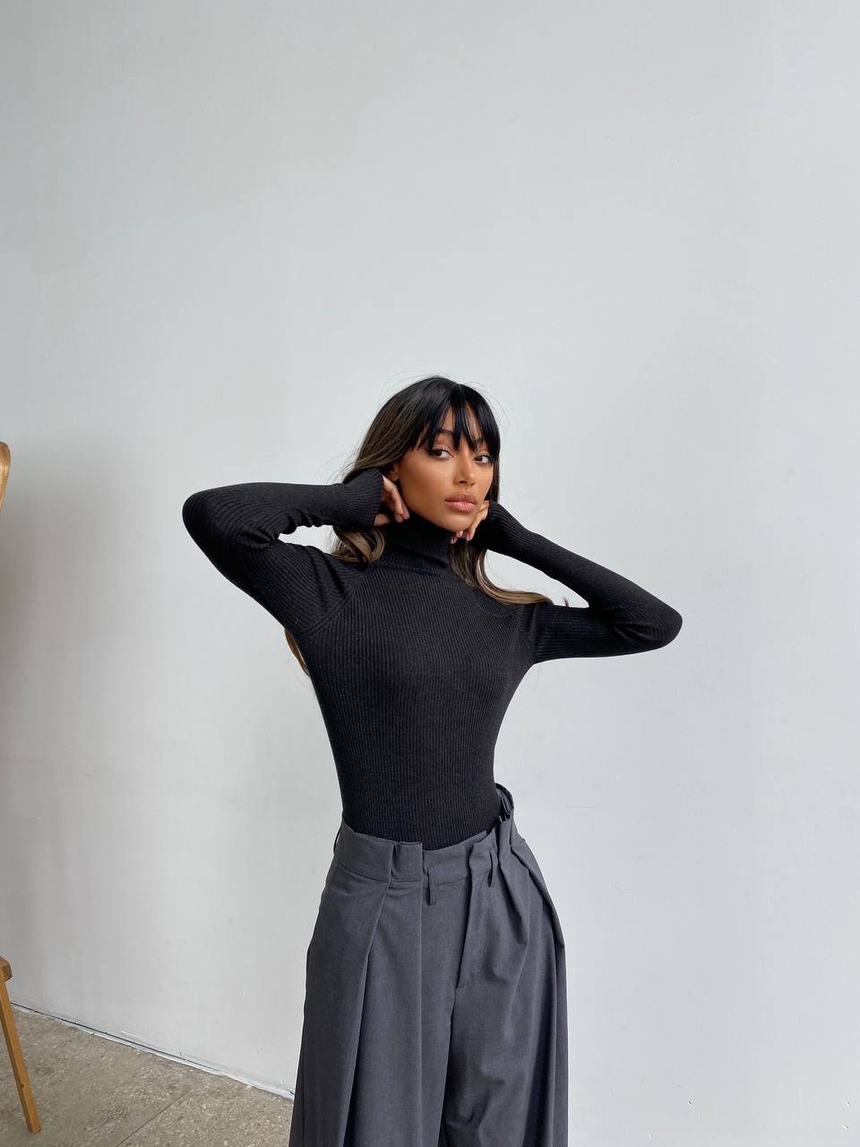 Person wearing a black turtleneck and gray pants against a plain background