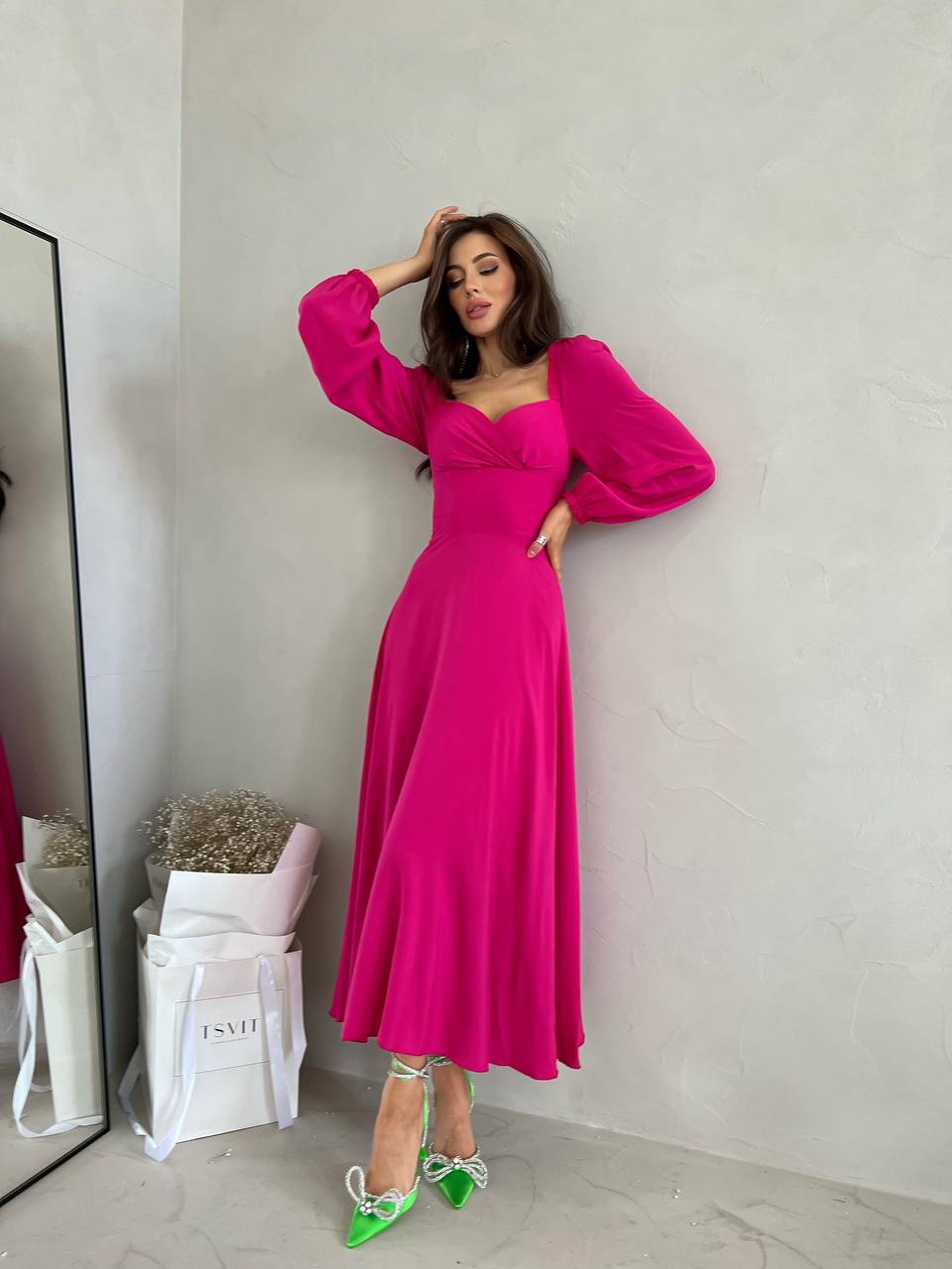 Woman in a bright pink dress standing against a plain wall.