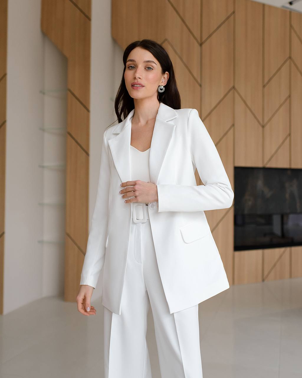 Woman wearing a white suit standing in a modern indoor setting.