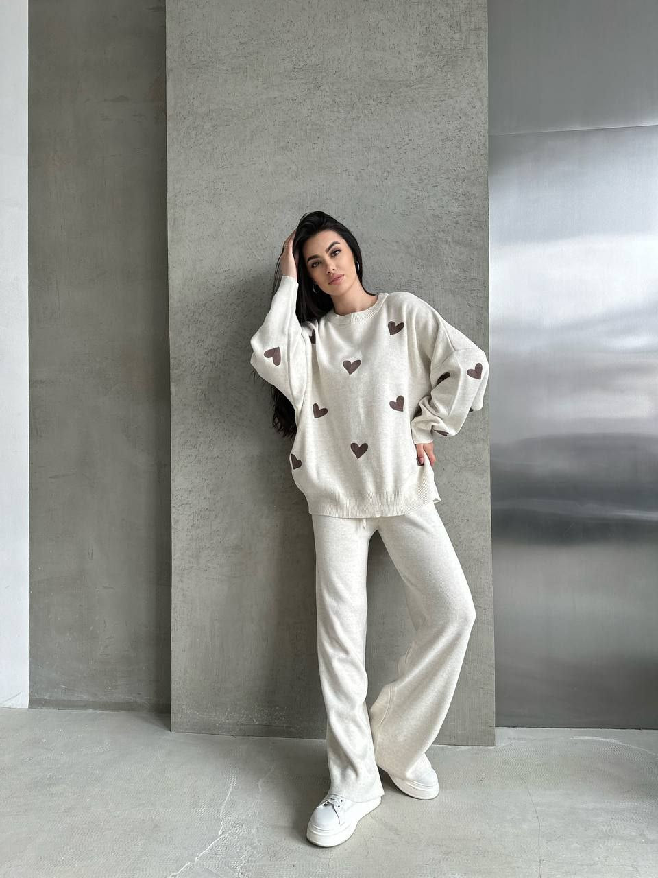 Woman wearing a white outfit with heart patterns against a gray wall.