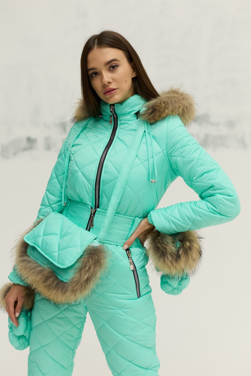 Woman wearing a turquoise winter outfit with fur trim against a light background