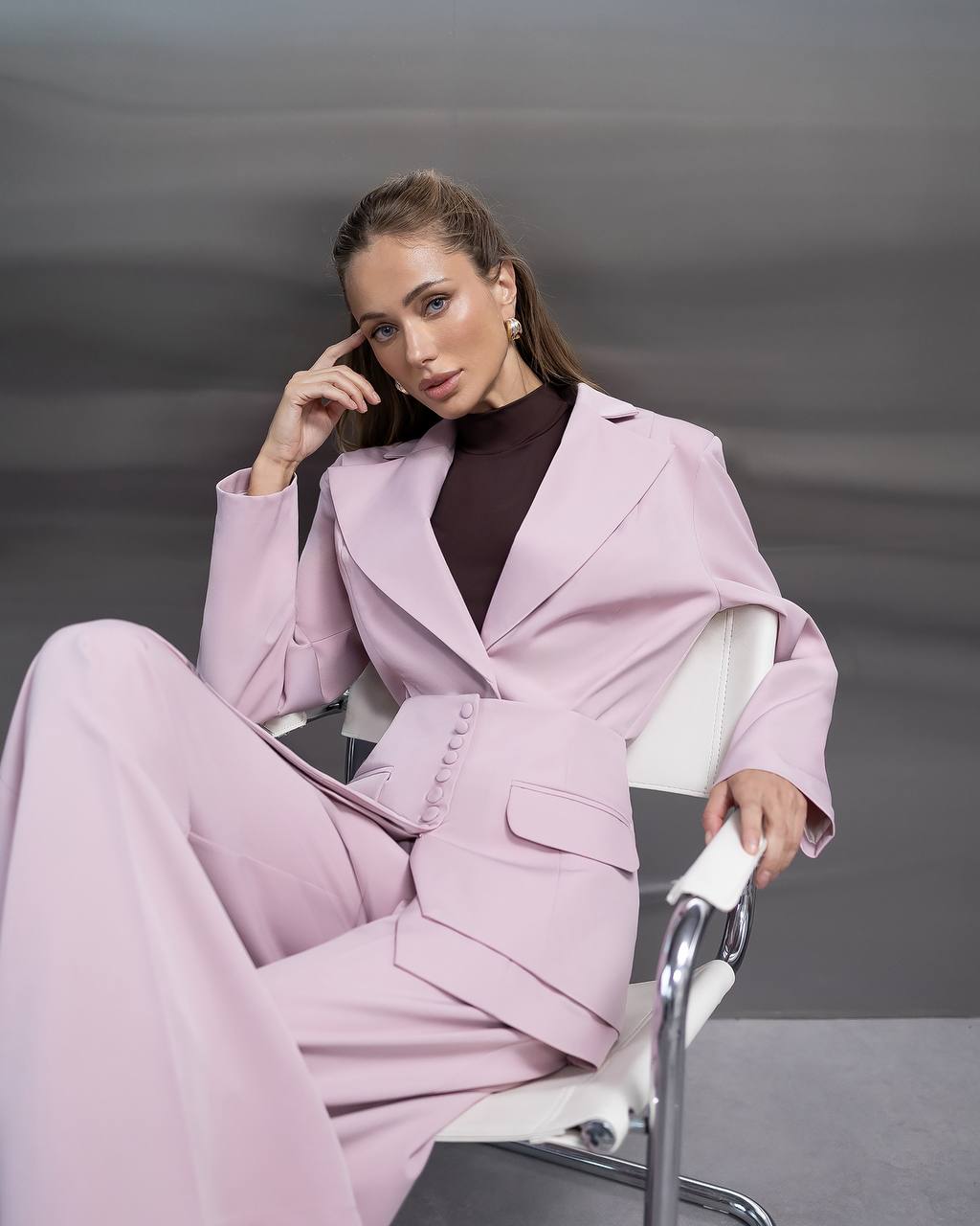 Woman in a pink suit sitting on a chair against a gray background