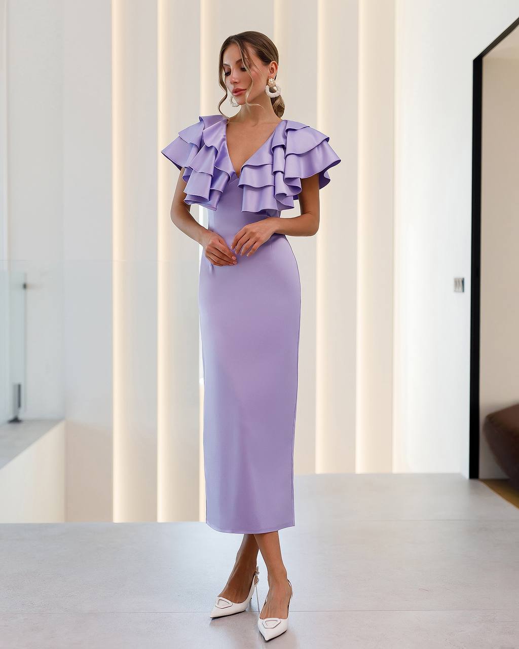 Woman wearing a lavender dress with ruffled details in a minimalistic setting.