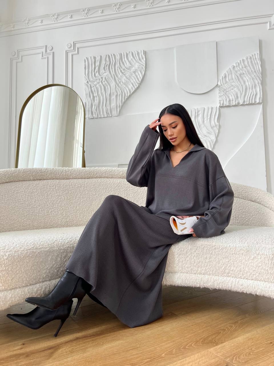 Woman in a gray dress sitting on a beige sofa in a stylish room.