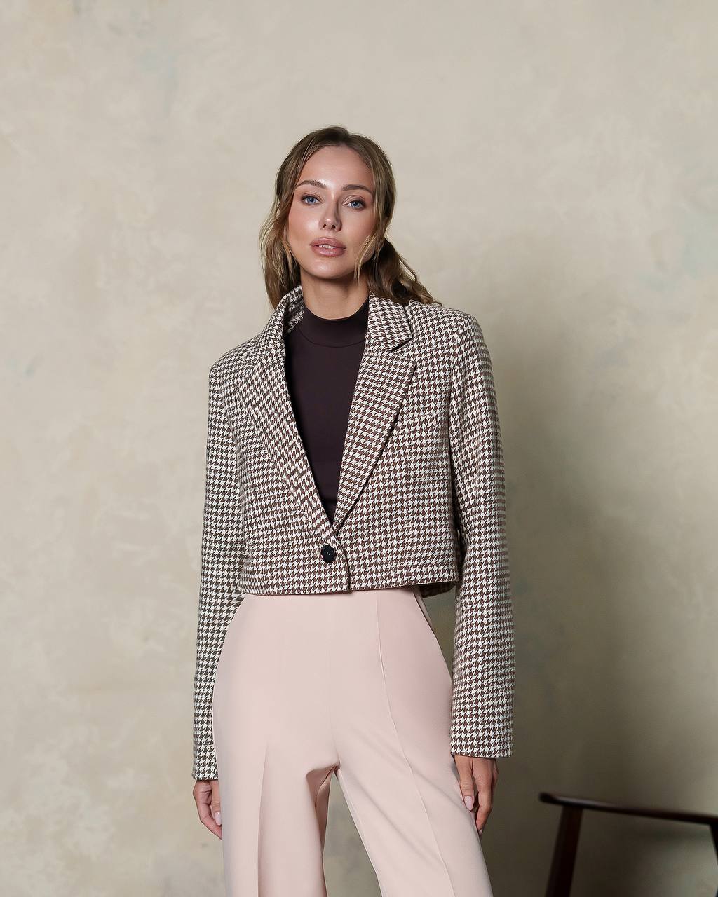 Woman wearing a checkered blazer and light pants against a neutral background