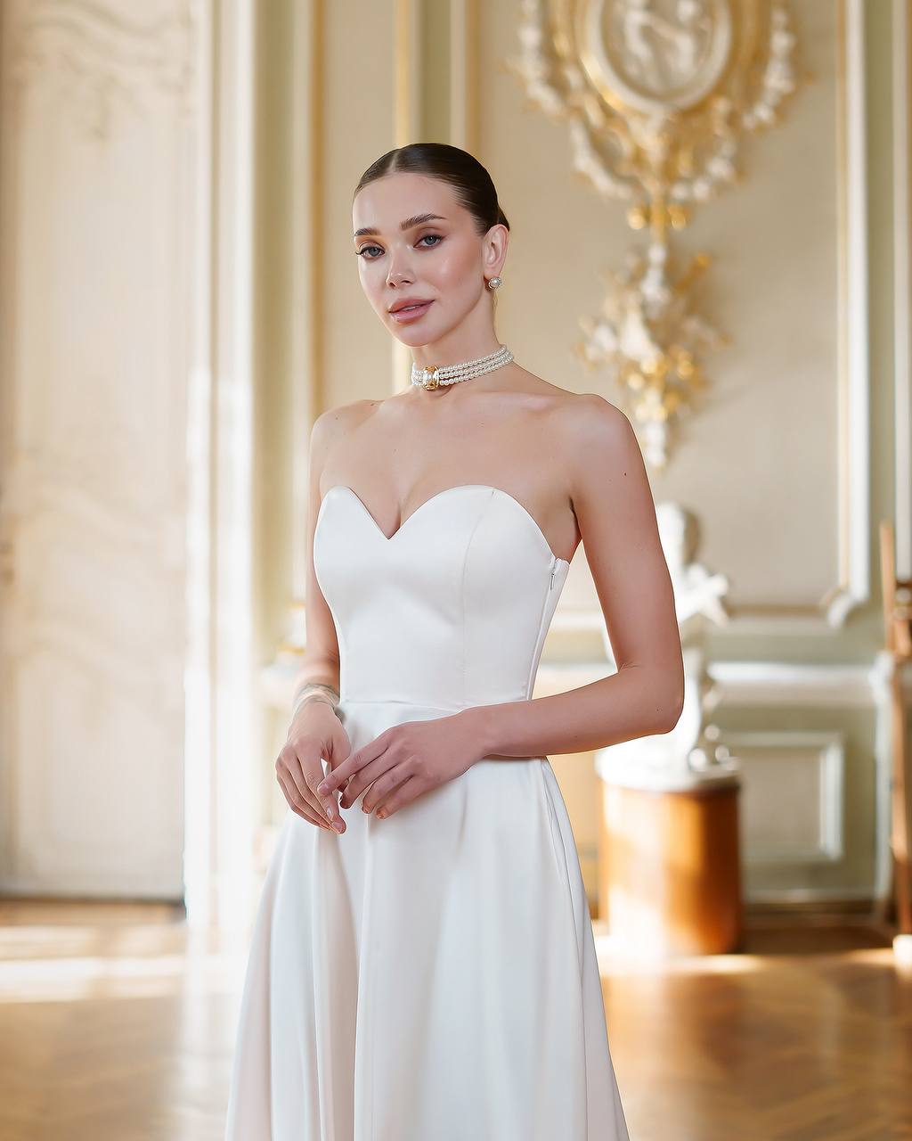 Woman in a white strapless dress standing in an elegant room with decorative elements.