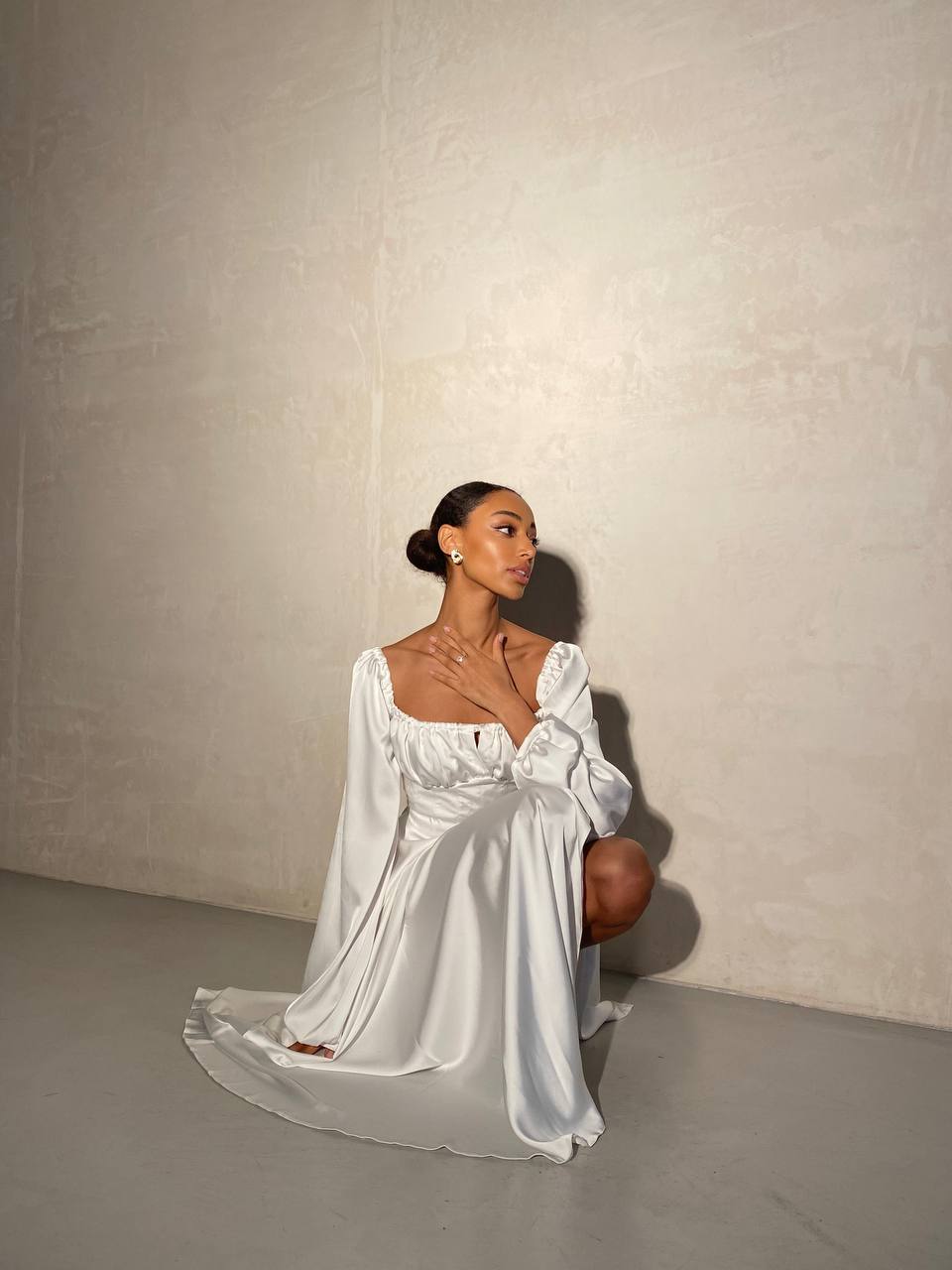 Woman in a white dress sitting against a plain background