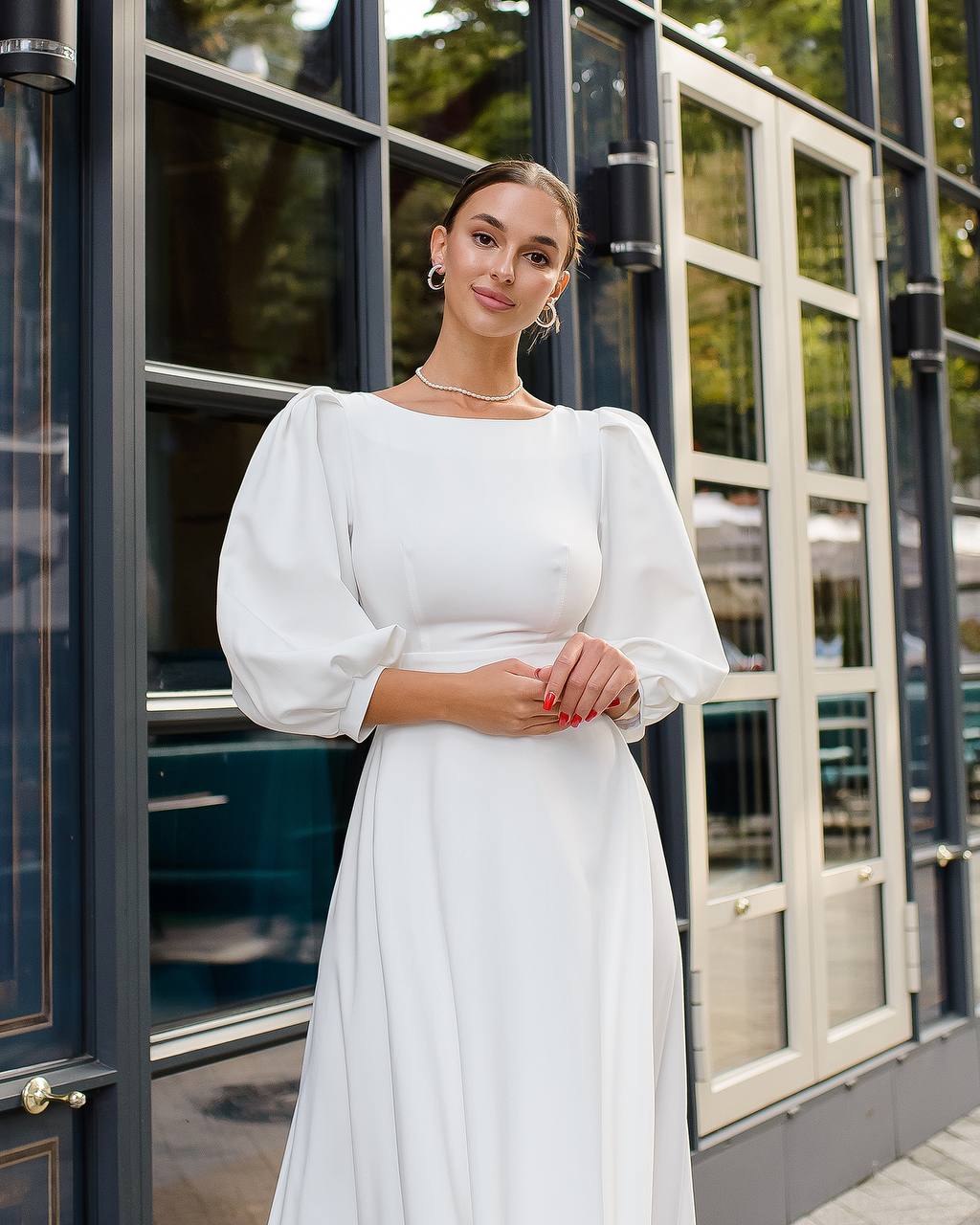 Woman in a white dress standing in front of a building with large windows.