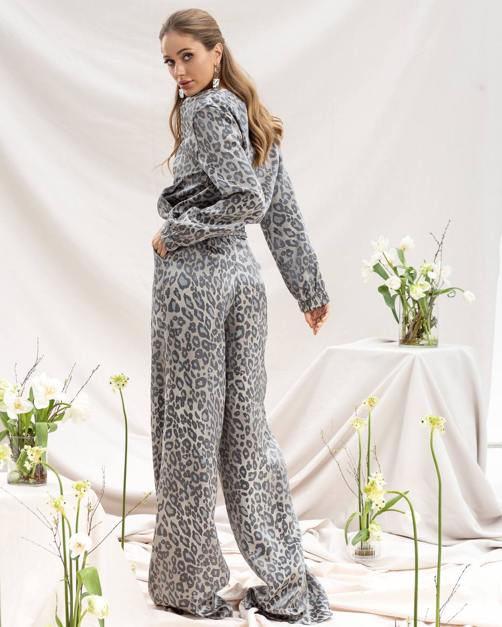 Woman wearing a leopard print outfit in a room with flowers and a tablecloth.