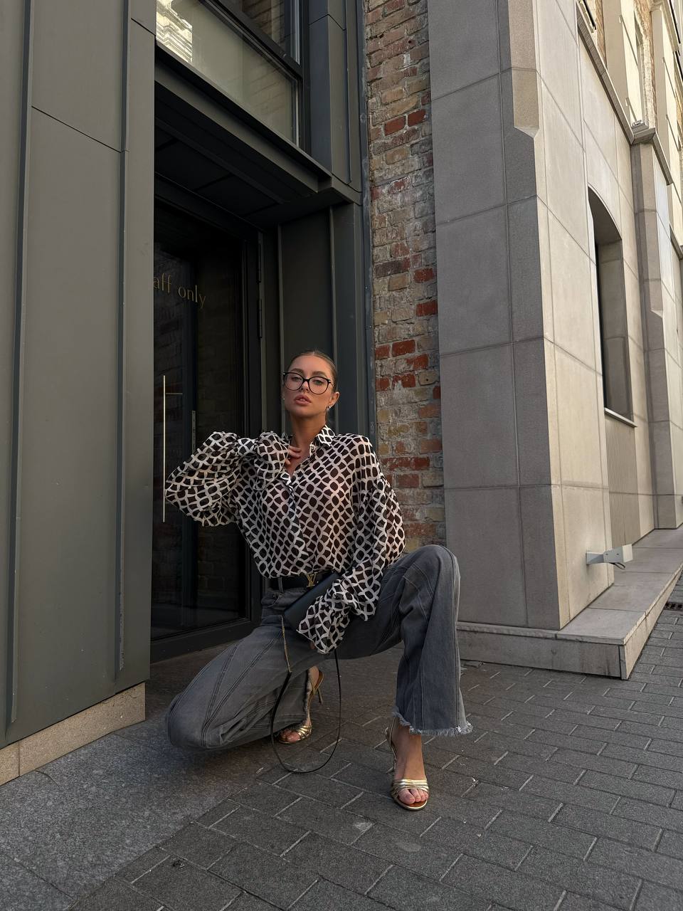 Woman posing on a city street wearing a patterned top and jeans.