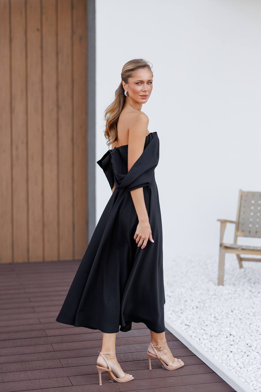 Woman in a black off-shoulder dress standing outdoors on a wooden deck.
