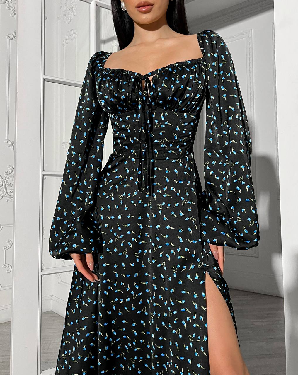 Woman wearing a black dress with blue floral pattern in a room with white walls.