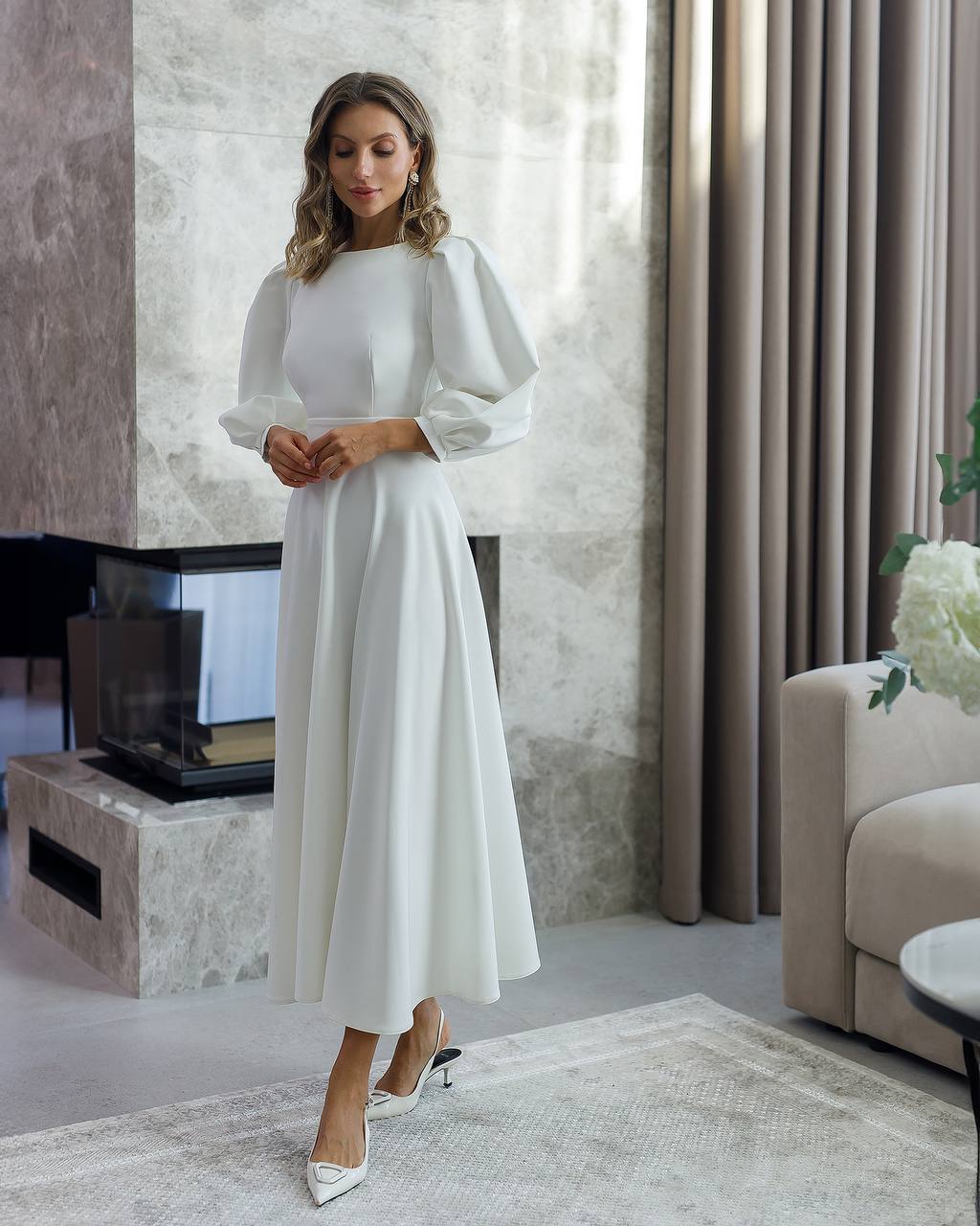 Woman in a white dress standing in a modern living room.