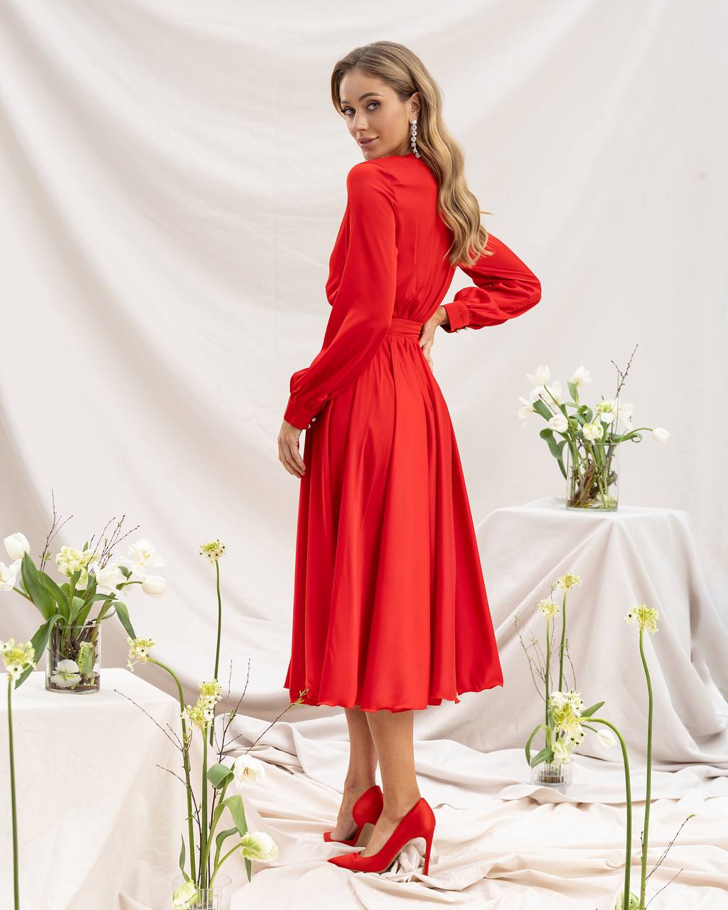 Woman in a red dress standing in a decorated room with flowers and white tablecloths.