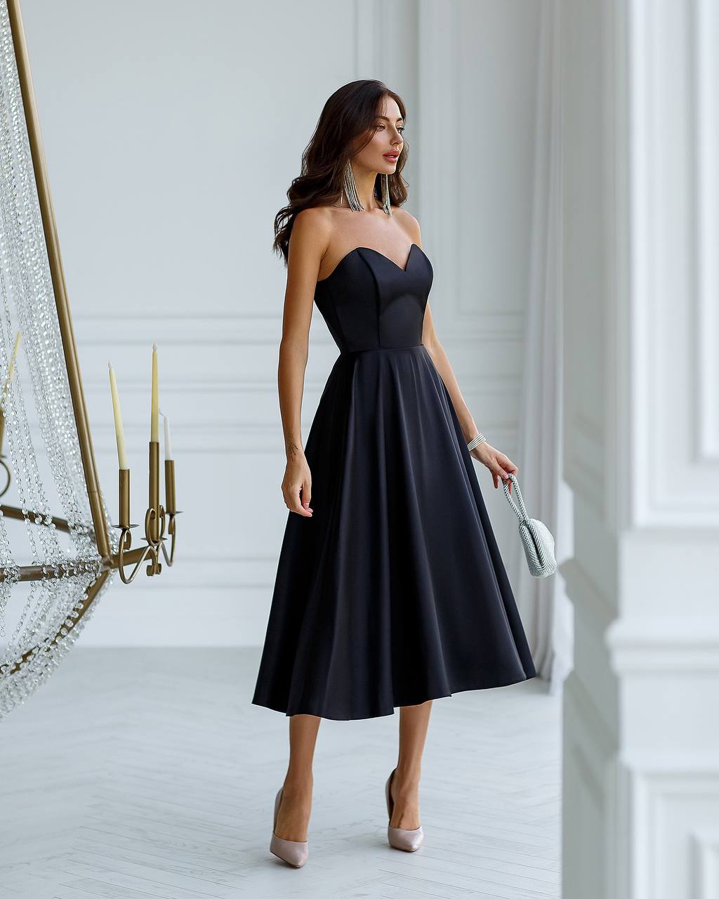 Woman in a black strapless dress standing in a stylish interior setting.
