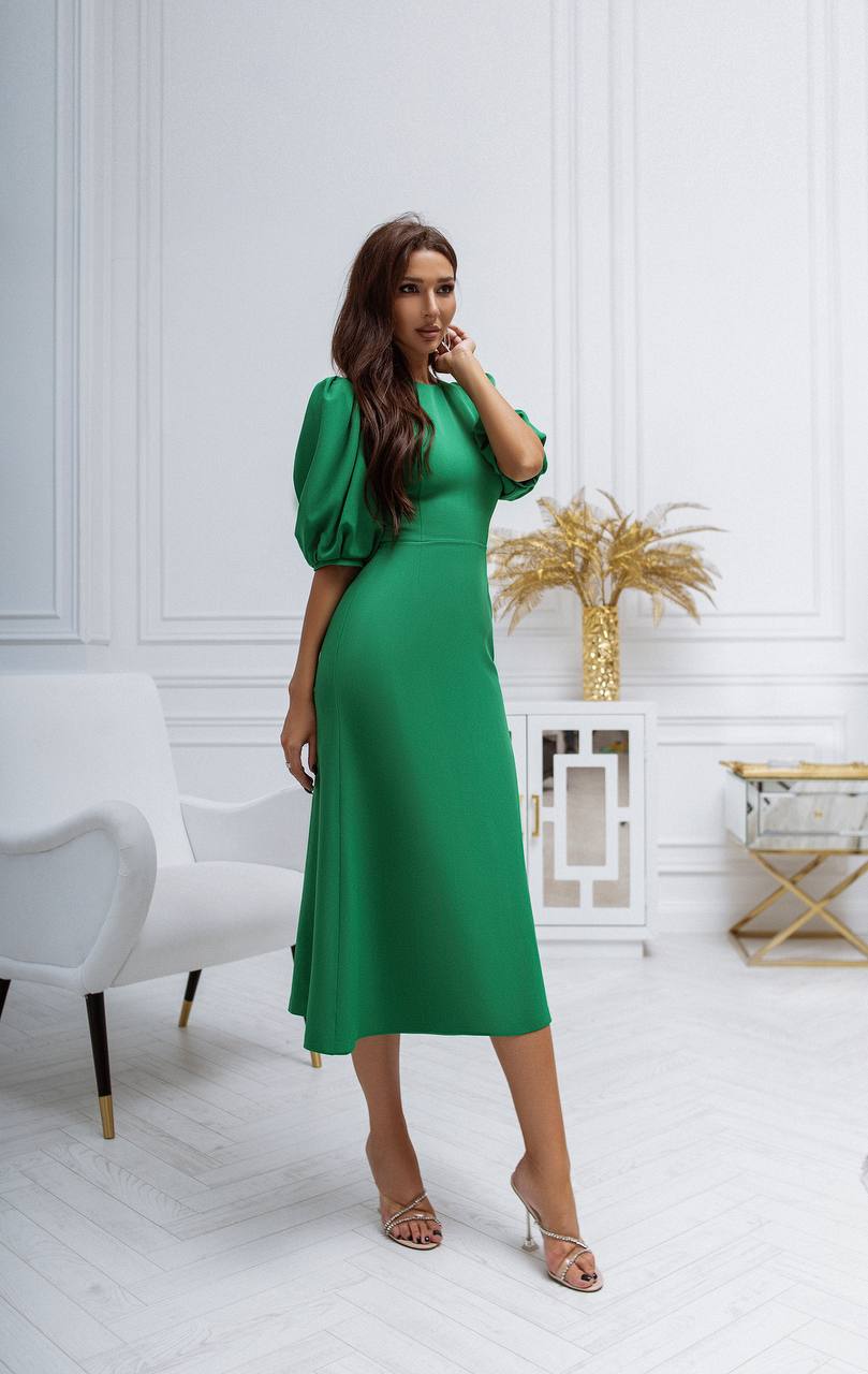 Woman in a green dress standing in a stylish room with white walls and decor.