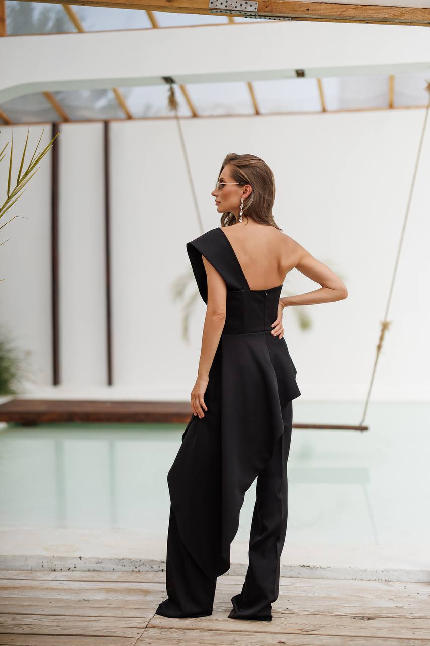 Woman wearing a black one-shoulder jumpsuit standing on a wooden deck.