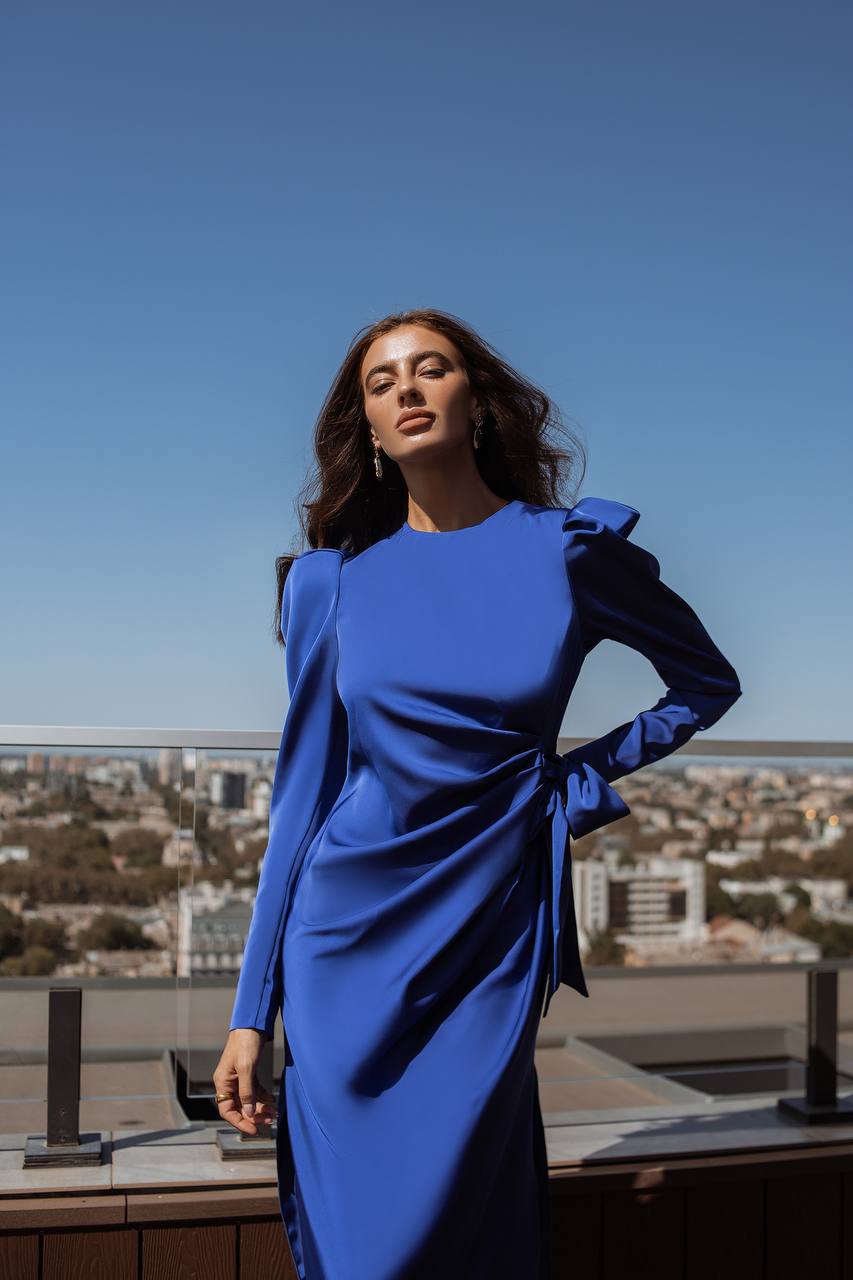 Woman in a blue dress standing on a rooftop with a cityscape in the background