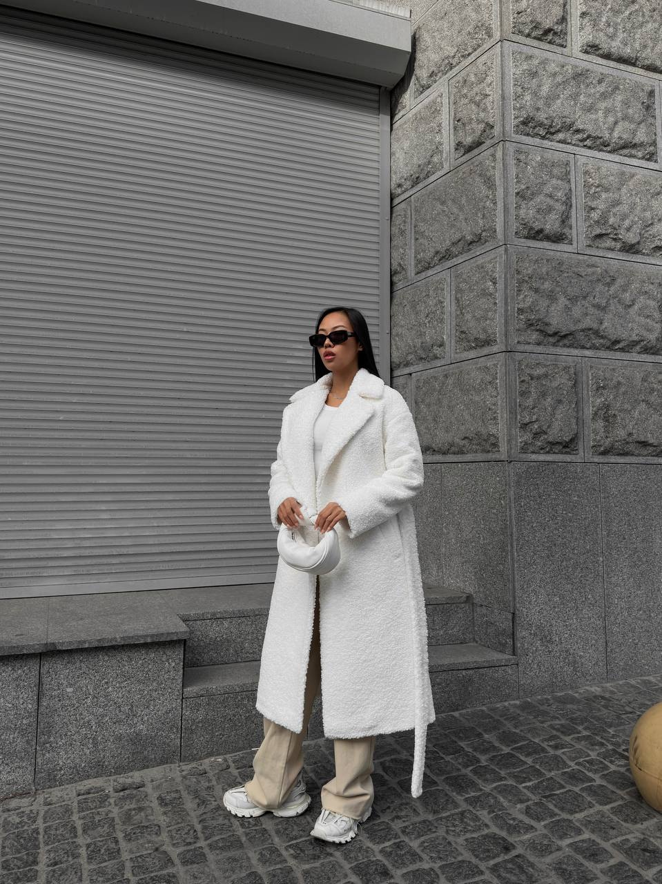 Person wearing a white coat standing in front of a gray building.