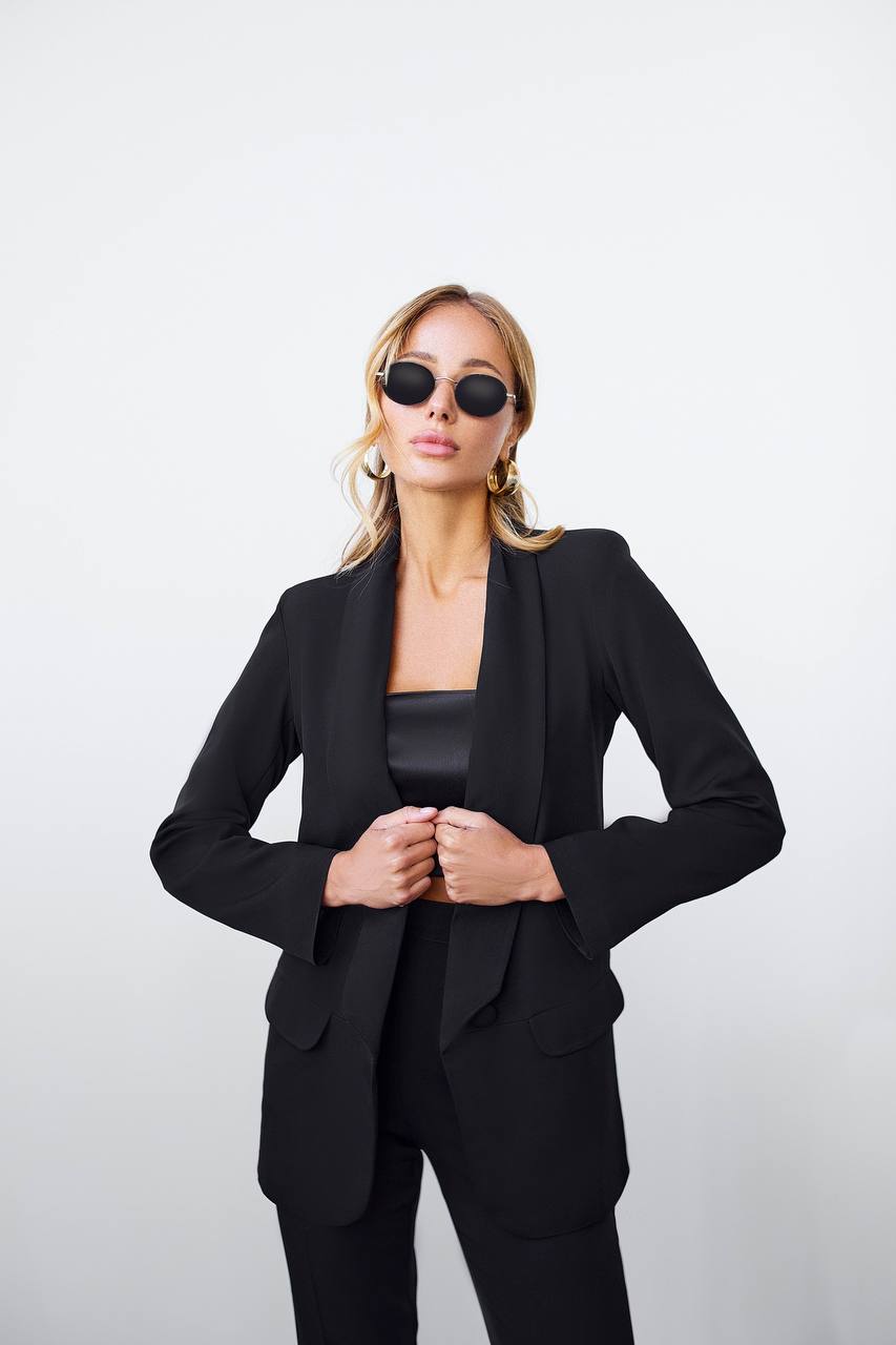 Woman wearing a black suit and sunglasses against a white background