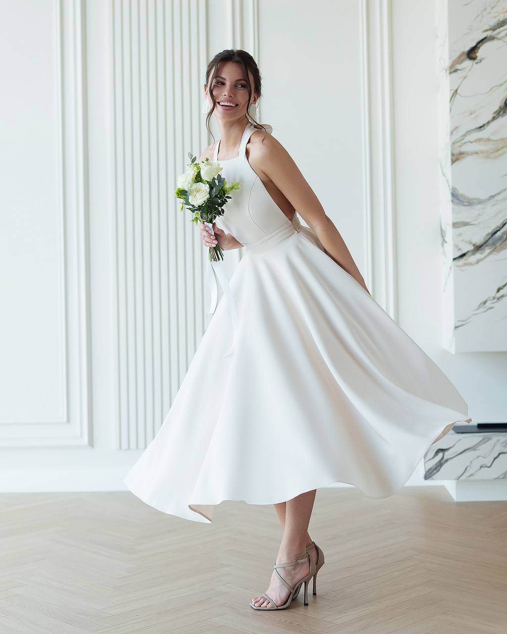 Woman in a white dress holding a bouquet in a room with marble walls.