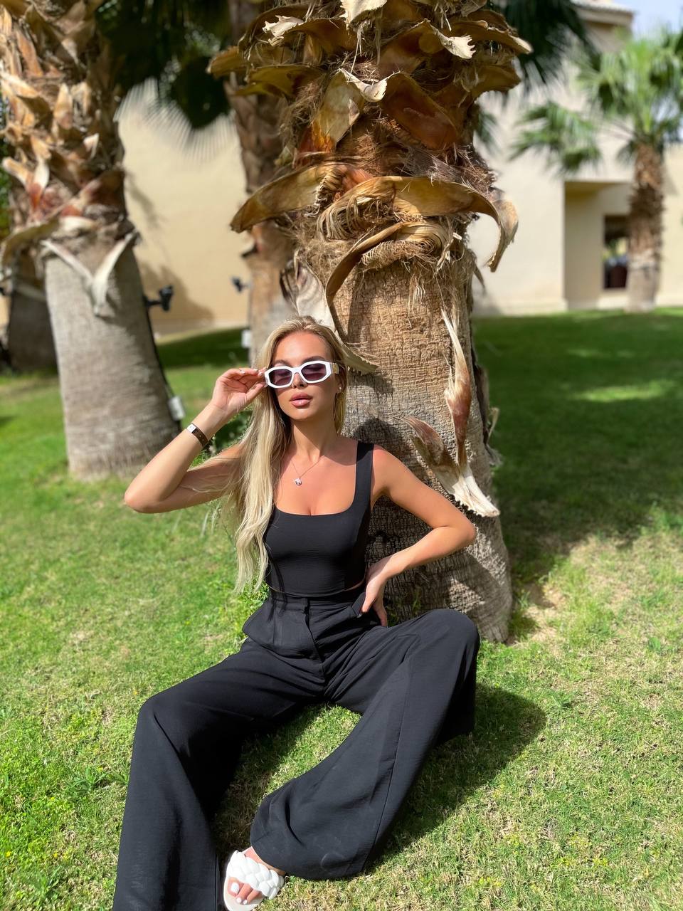 Woman in a black outfit posing outdoors with palm trees in the background