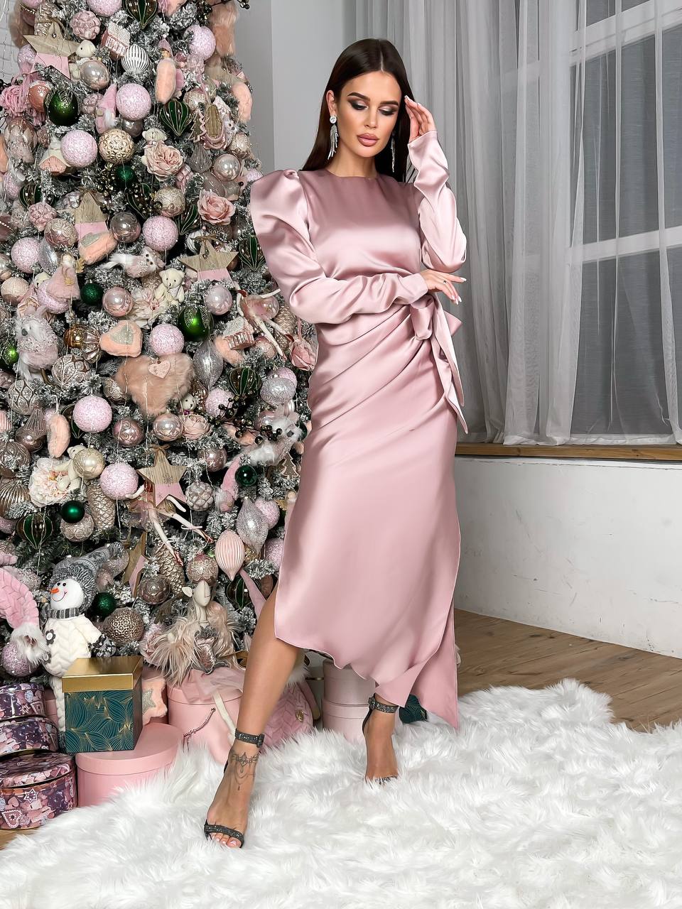 Woman in a pink dress standing next to a decorated Christmas tree indoors.