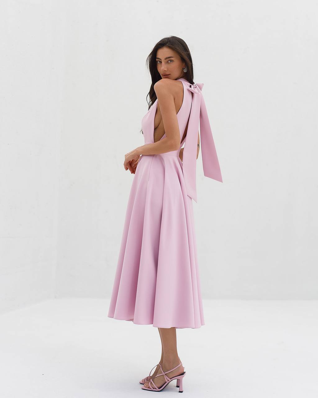 Woman wearing a pink dress with a bow detail on a white background