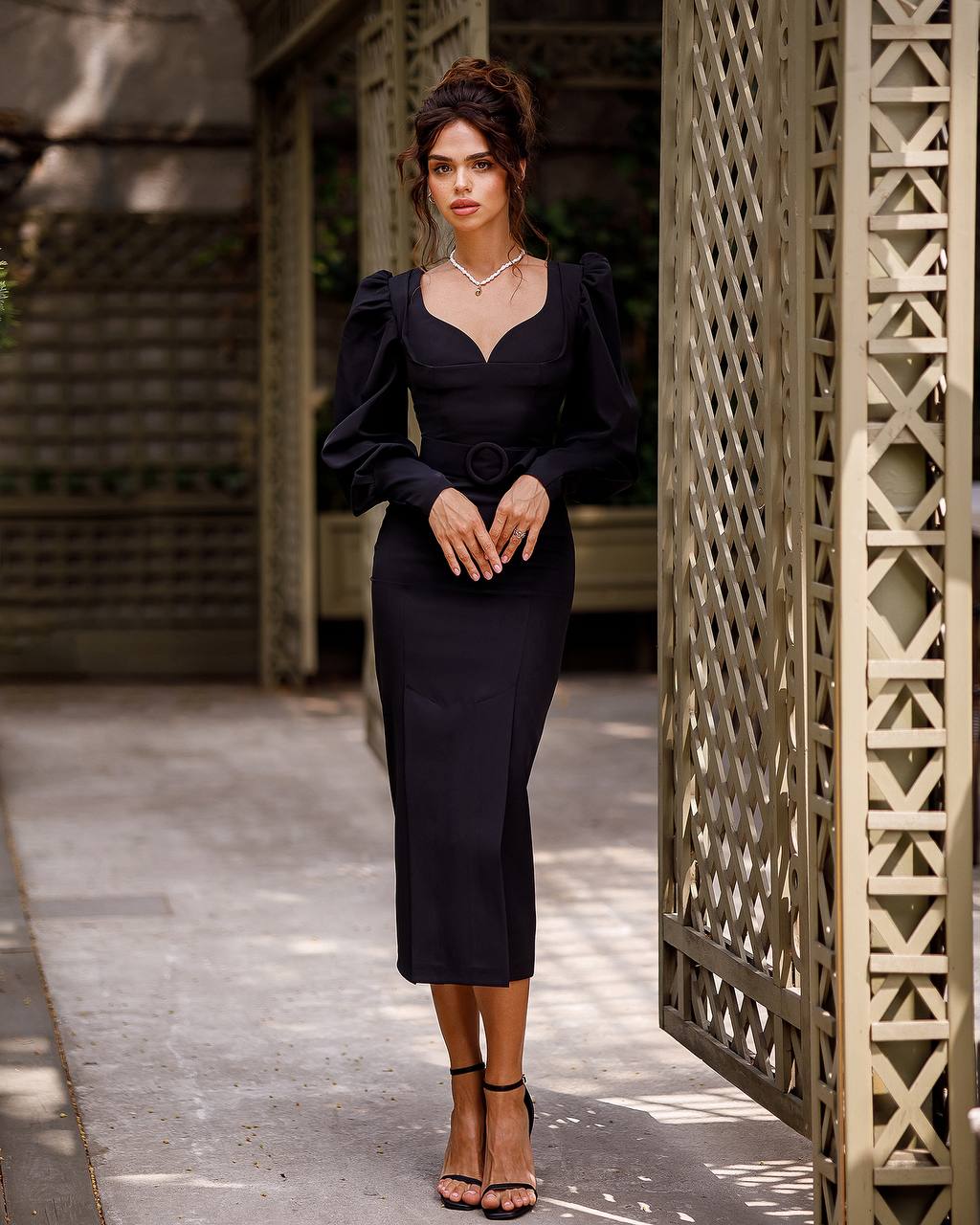 Woman in a black dress standing in front of a textured wall.