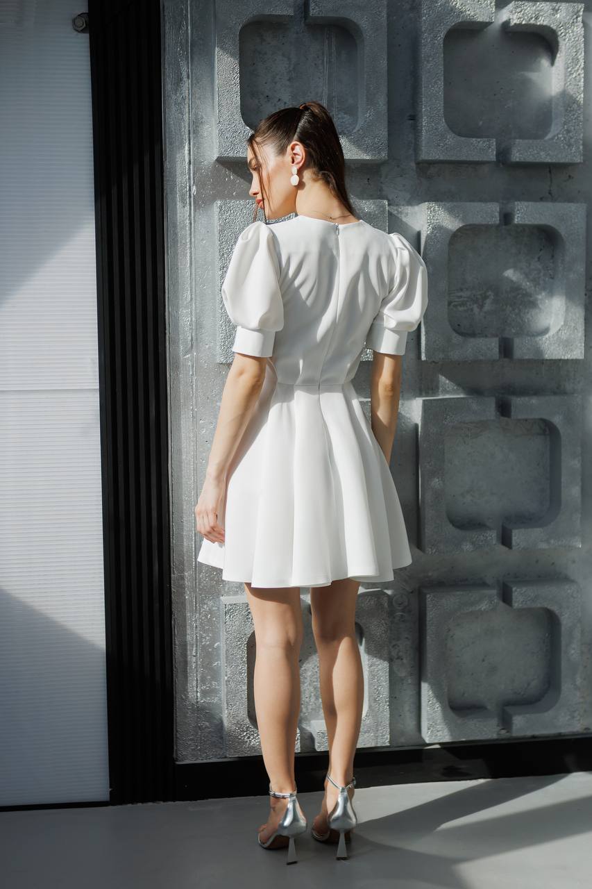 Woman in a white dress standing against a textured wall.