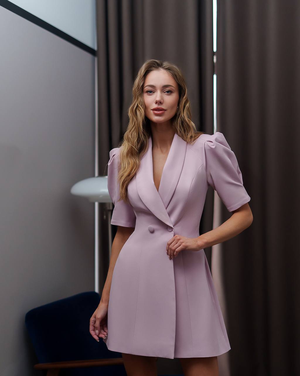 Woman wearing a light purple dress standing indoors with neutral background