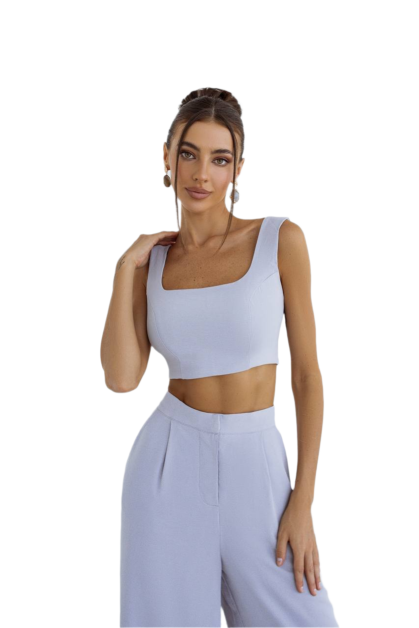 Woman wearing a light blue sleeveless top and high-waisted pants on a white background