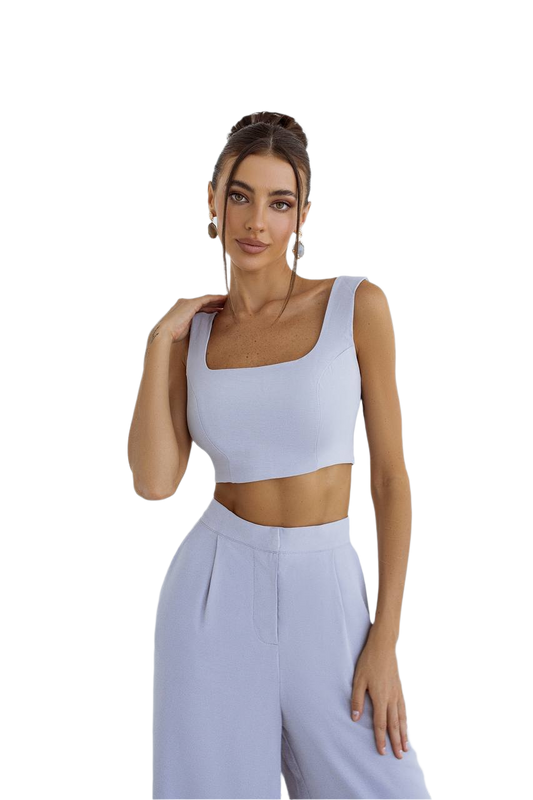 Woman wearing a light blue sleeveless top and high-waisted pants on a white background