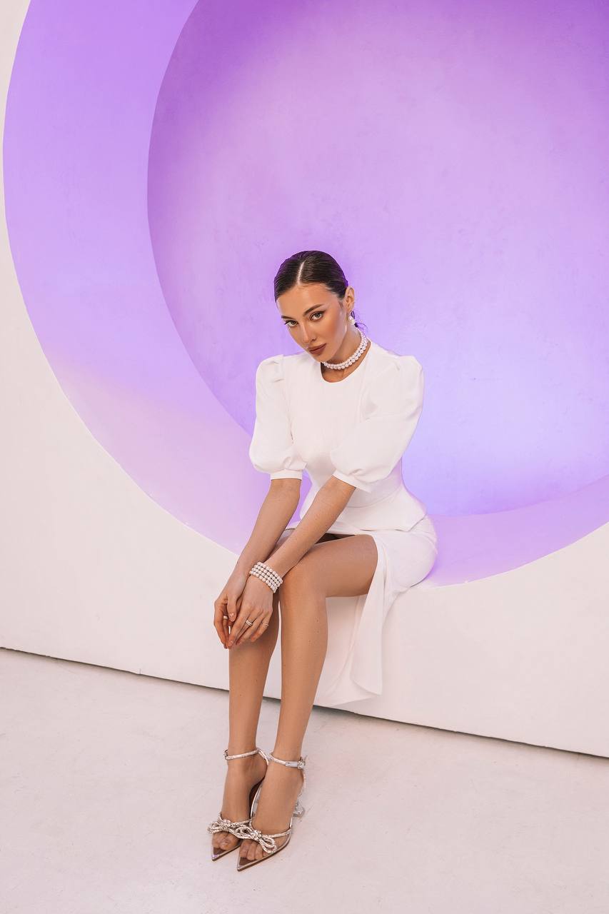 Woman in a white dress sitting against a purple and white abstract background