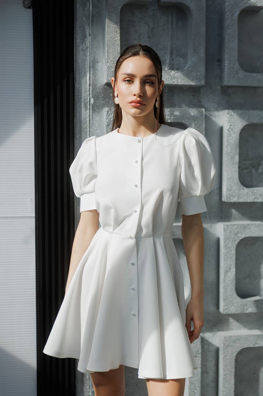 Woman wearing a white dress standing against a textured wall.