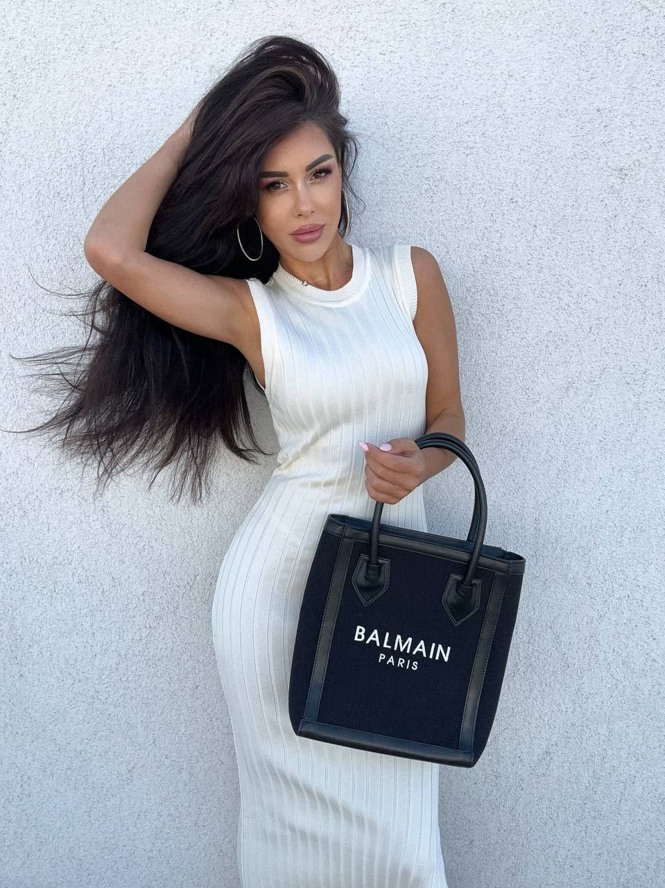 Woman holding a Balmain black handbag against a light background