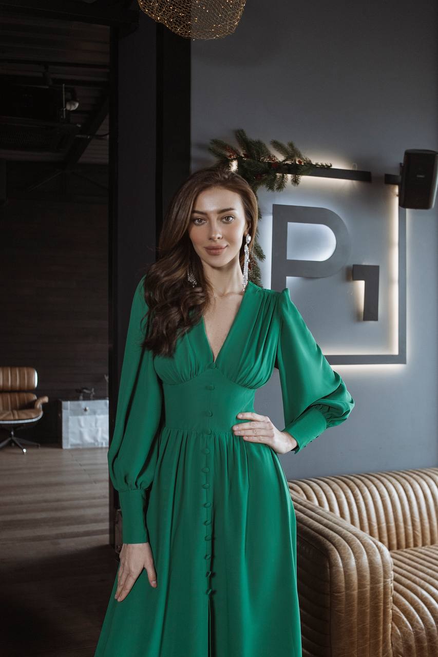 Woman in a green dress standing in an indoor setting with a modern interior design.